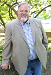 Ken McVicker posing outside in a tan blazer and blue shirt.