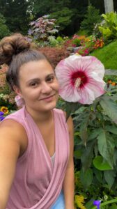 Woman in pink shirt smiling next to a pink hibiscus flower