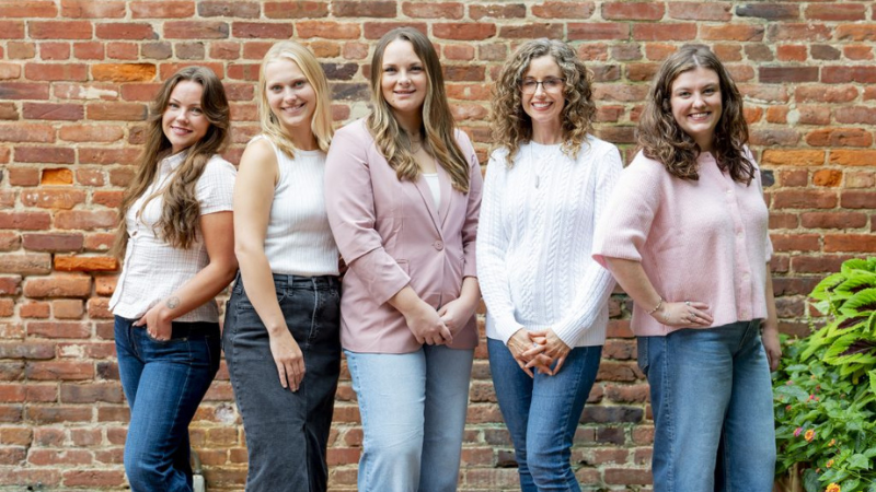 Five women posing in front of a brick wall.
