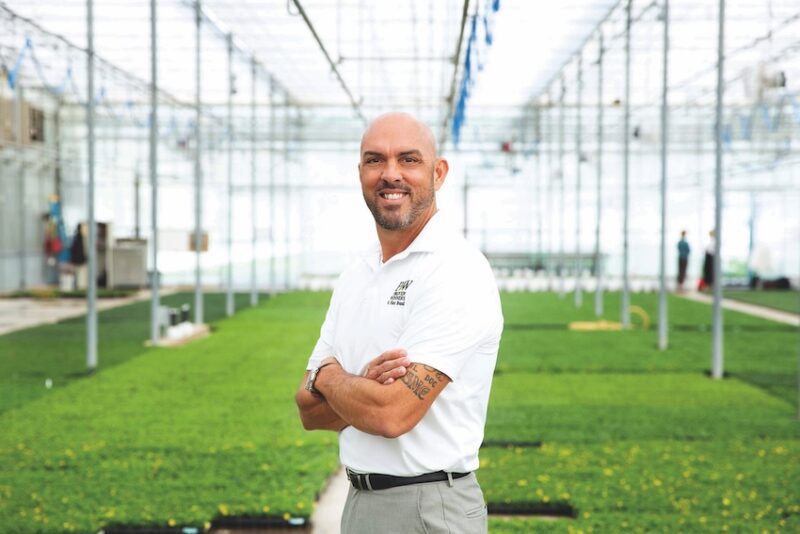 man standing in a greenhouse with arms crossed and smiling
