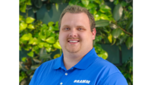 man in blue shirt smiling with green leaves in the background
