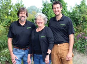 Two men and a women standing in the middle, smiling for a photo outside