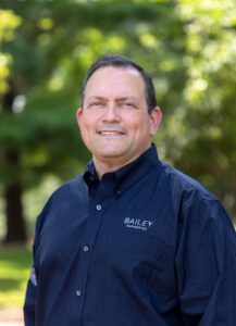 A smiling man standing outside with trees in the background