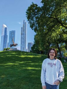 A man standing on a green hill with tall buildings in the background