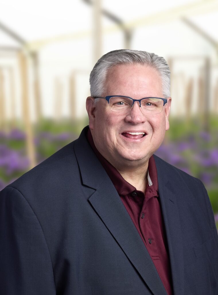 headshot of smiling man with greenhouse background