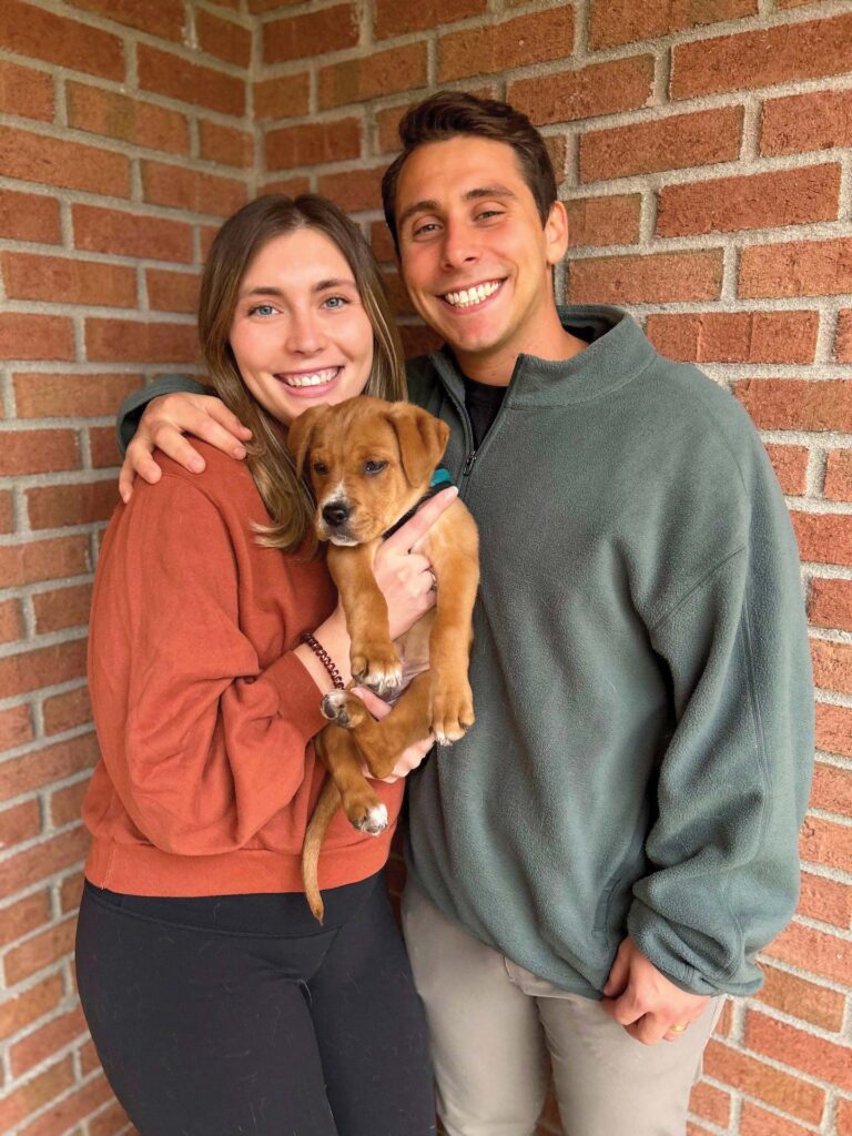 man with arm around woman holding a dog