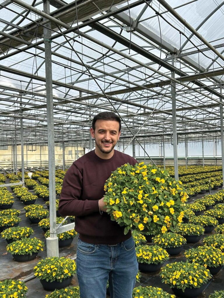 man in greenhouse holding flowering potted plant