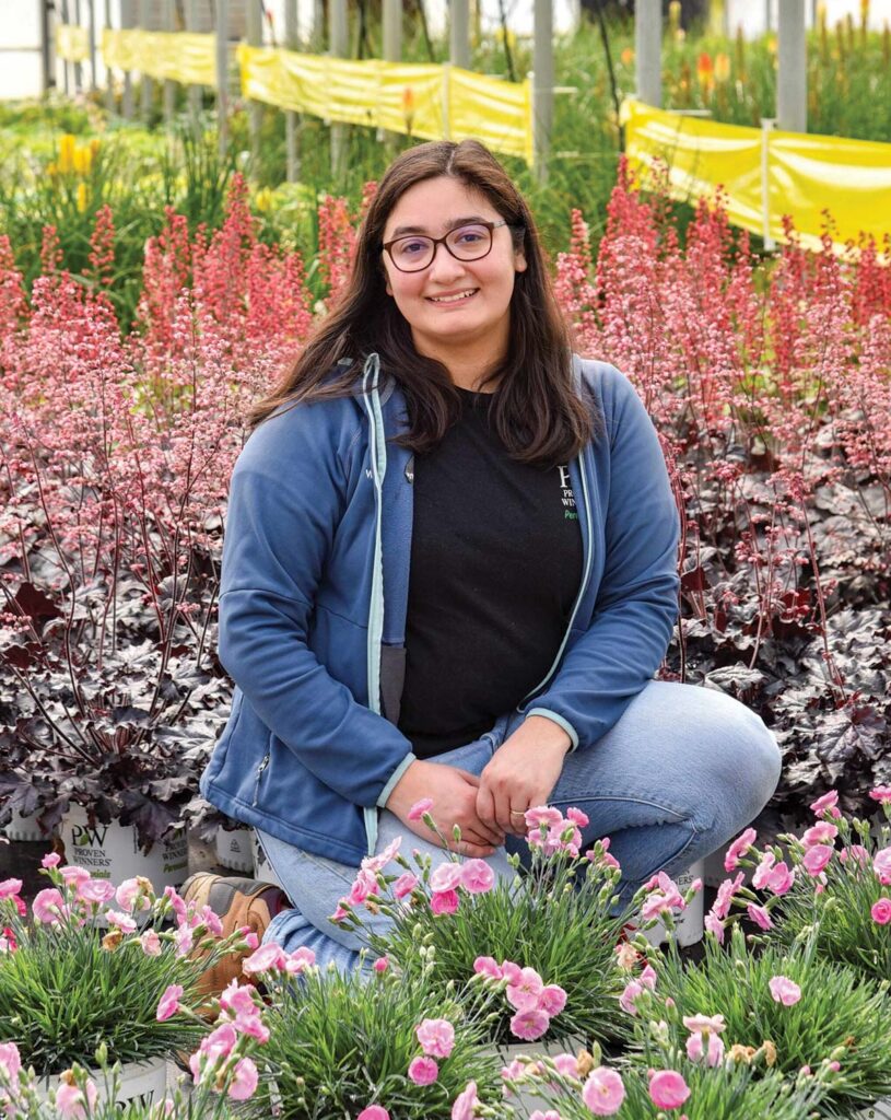 smiling woman squatting among flowering plants
