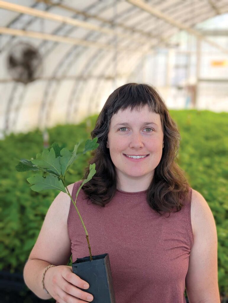 woman in hoop house holding small potted plant