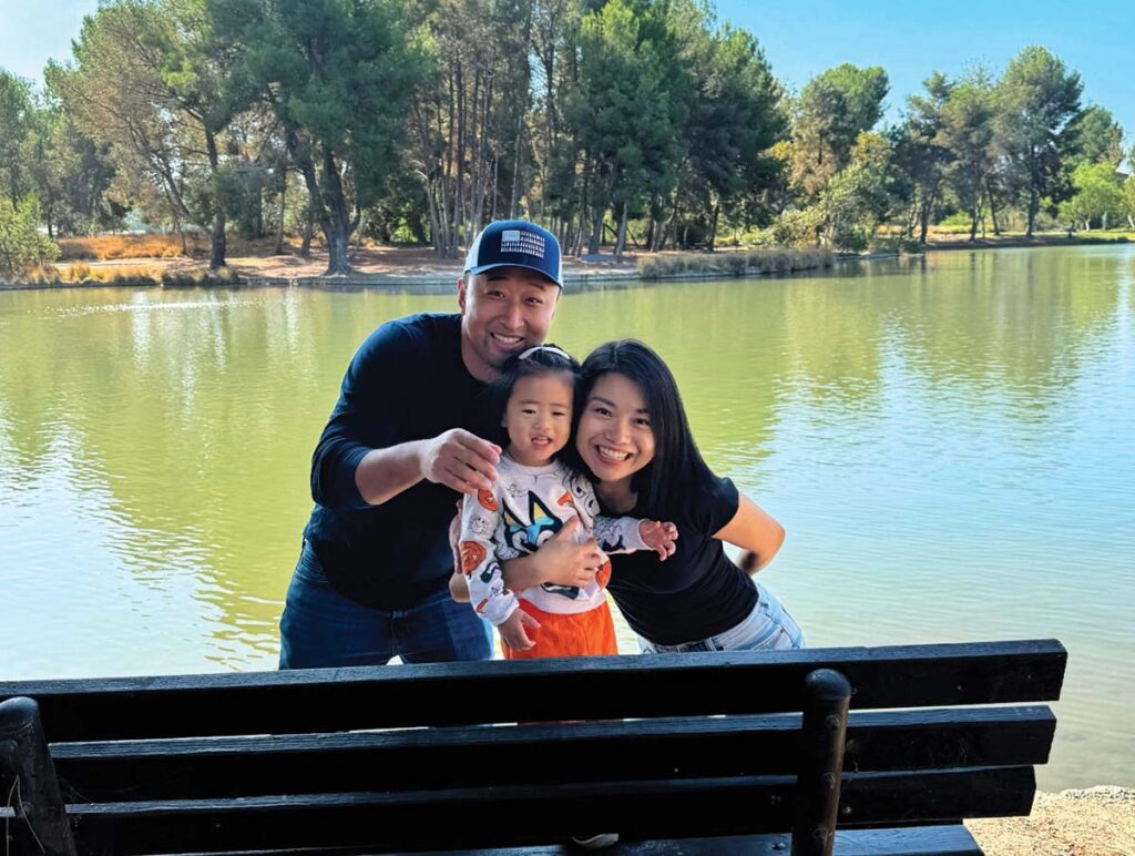 man, woman and child posing with pond in background